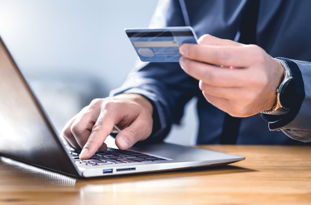 Een man in pak houdt een pinpas bij zijn computer om het nummer over te nemen voor een online betaling van het voorschot voor een opdracht die hij geeft.