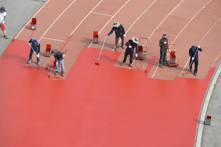 Zeven arbeiders die een atletiekbaan schilderen